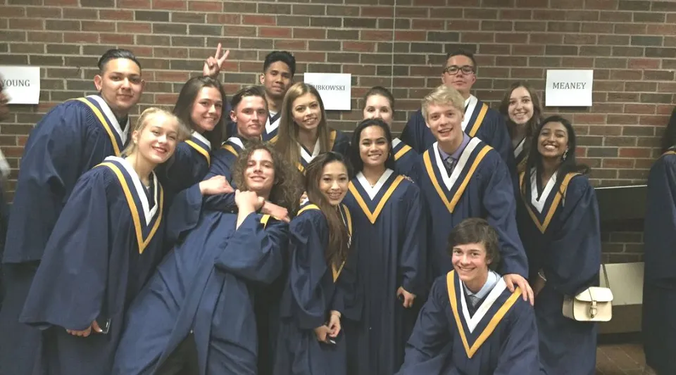 Un gruppo di diplomati nell'abito da cerimonia della Notre Dame High School a Calgary posa davanti a una parete in mattoni.