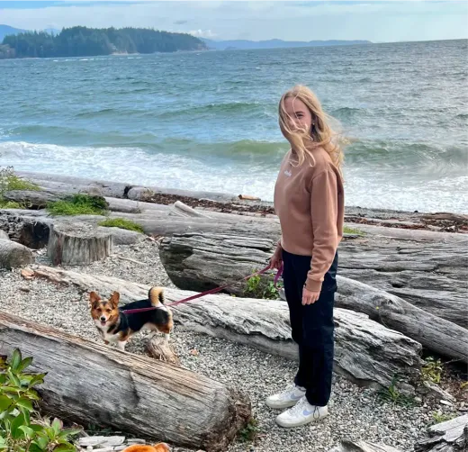 Lina Marie geht mit einem kleinen Hund über einen Kiesstrand am Meer in Kanada