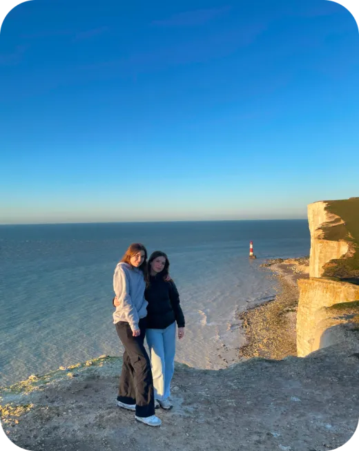 Zwei Mädchen posieren auf den weißen Kreidefelsen, im Hintergrund ein Leuchtturm in England