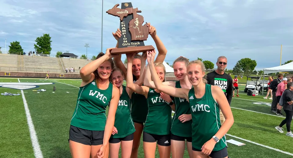 Studenti della Western Michigan Christian School festeggiano con un trofeo sul campo sportivo davanti a uno stadio.