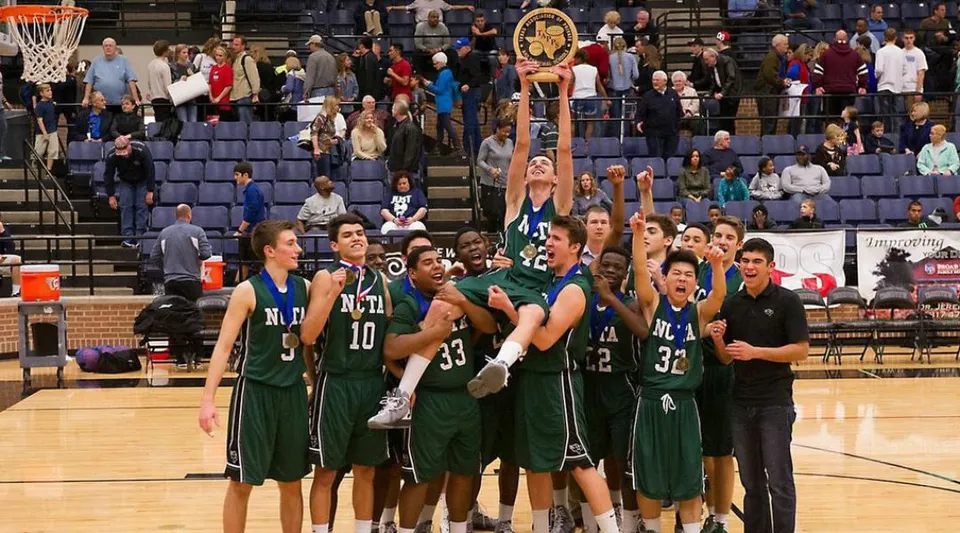 Un gruppo di giocatori di basket in maglia verde festeggia sul campo della North Central Texas Academy davanti al pubblico.