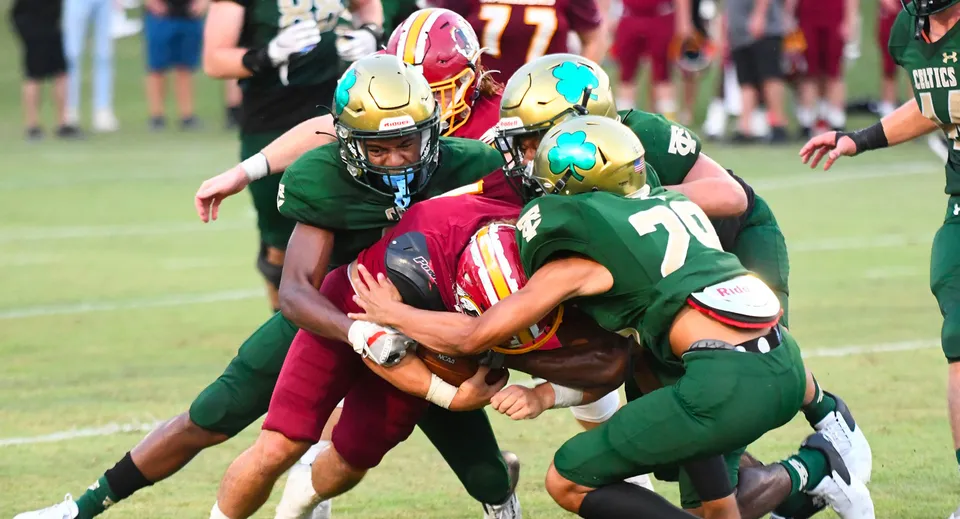 Studenti della Trinity Catholic High School eseguono un'intensa azione di tackle di football americano sul campo da gioco.
