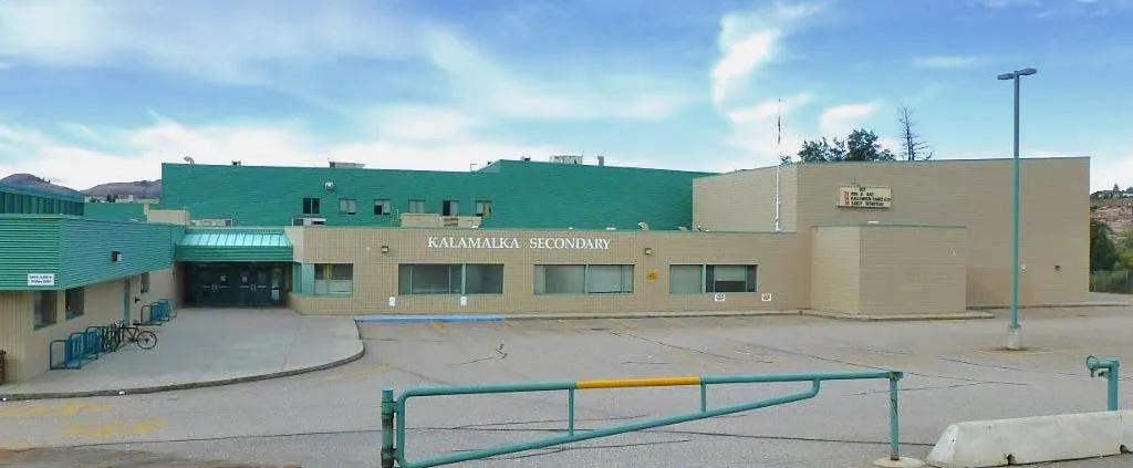 El edificio de varios pisos verde y beige de la Kalamalka Secondary School con un letrero visible y una zona pavimentada en primer plano.