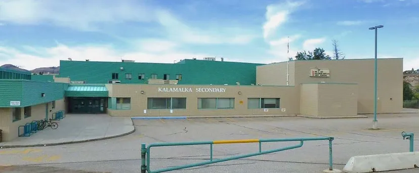 L'edificio a più piani verde e beige della Kalamalka Secondary School con la scritta ben visibile e un'area pavimentata in primo piano.