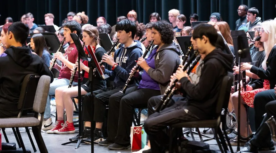 Studenti del Chandler Unified School District siedono in fila e suonano diversi strumenti musicali durante una prova di musica.