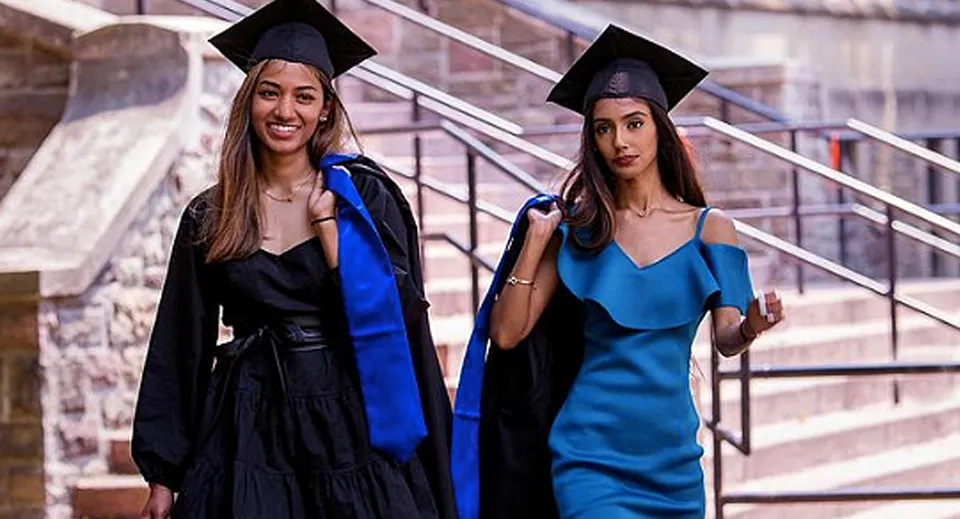 Due studentesse in toga da diploma posano su una scalinata davanti a un edificio in mattoni nel campus del Jarvis Collegiate Institute.