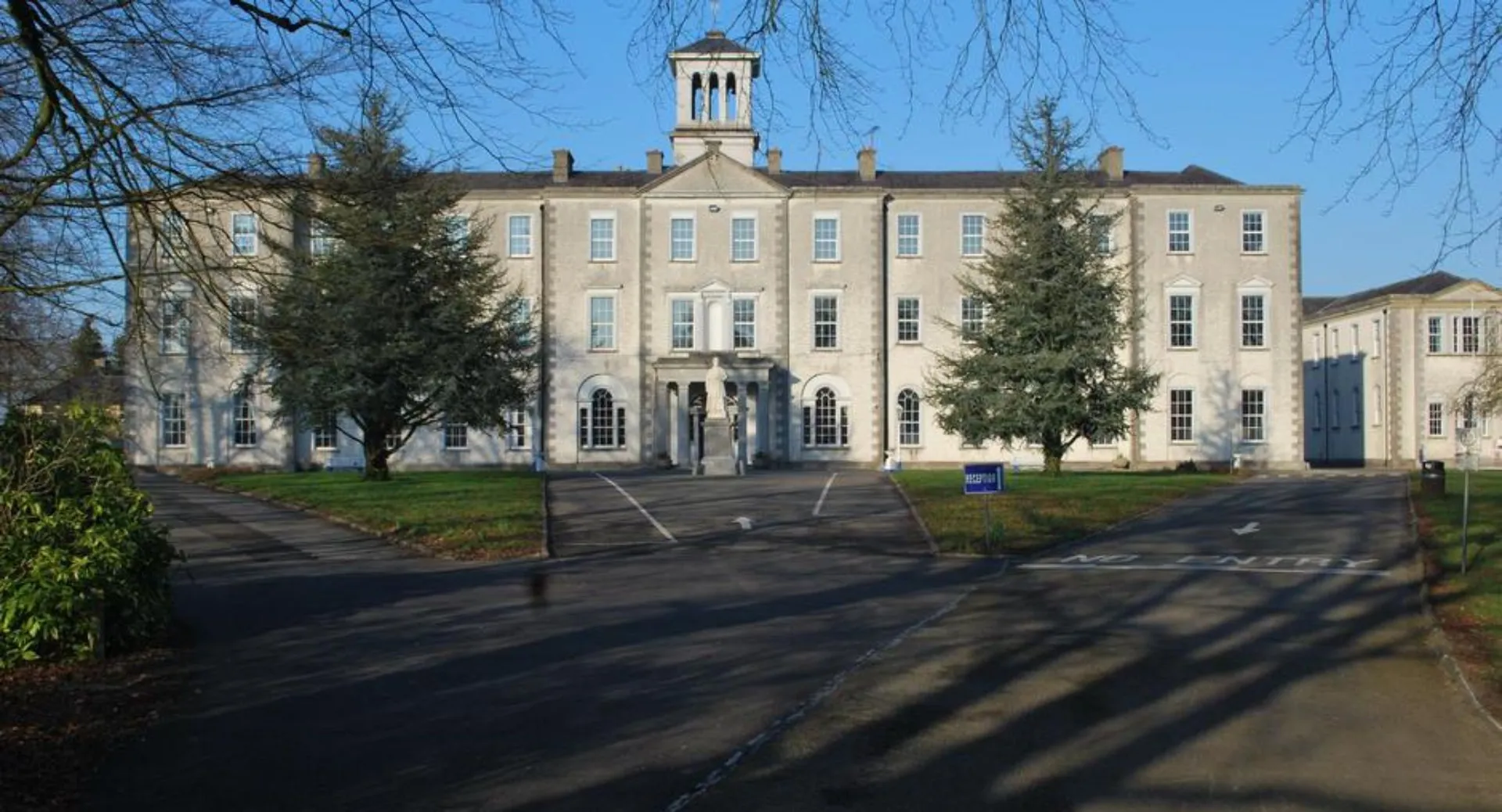 L'edificio in mattoni a più piani con un'imponente torre nel campus del St. Mel’s College è circondato da alberi.