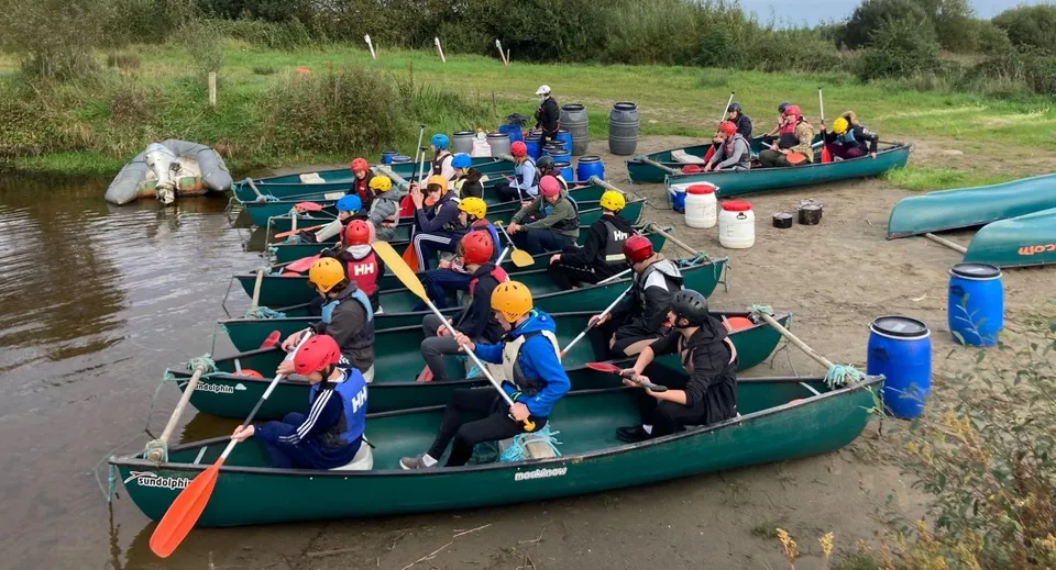 Studenti della Carrigallen Vocational School siedono su canoe con giubbotti di salvataggio colorati su un fiume dalla fitta vegetazione.