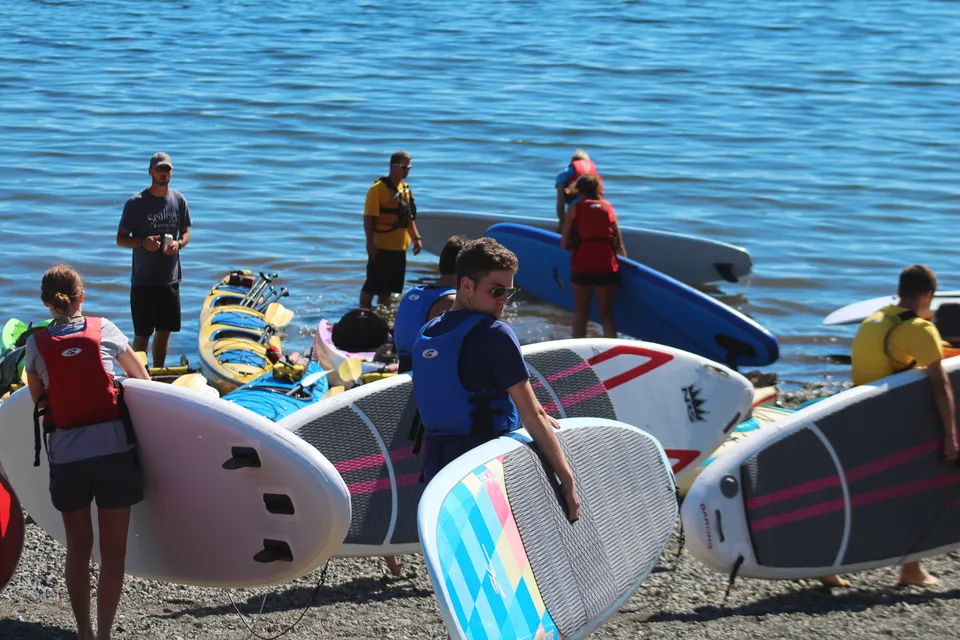 Studenti della Ladysmith Secondary School stanno su paddleboard in uno specchio d'acqua con uno sfondo blu.