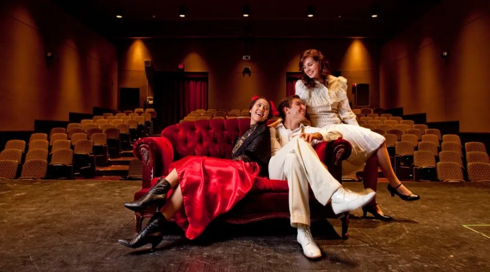 Un gruppo di donne vestite in modo elegante siede sul divano di velluto rosso nel teatro del College of the Desert.