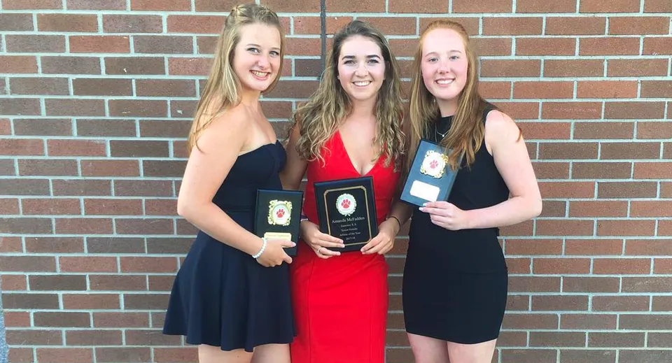 Tre studentesse della Eastview Secondary School sono in piedi davanti a una parete in mattoni e tengono in mano dei premi.