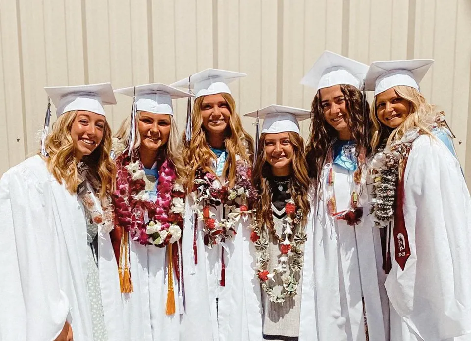 Un gruppo di giovani diplomate della Morgan High School è in piedi in abiti da laurea davanti a una parete in legno.