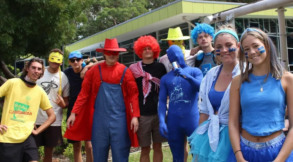 Un gruppo di studenti e studentesse della Barrenjoey High School indossa costumi colorati e si trova all'aperto davanti ad alberi ed edifici.