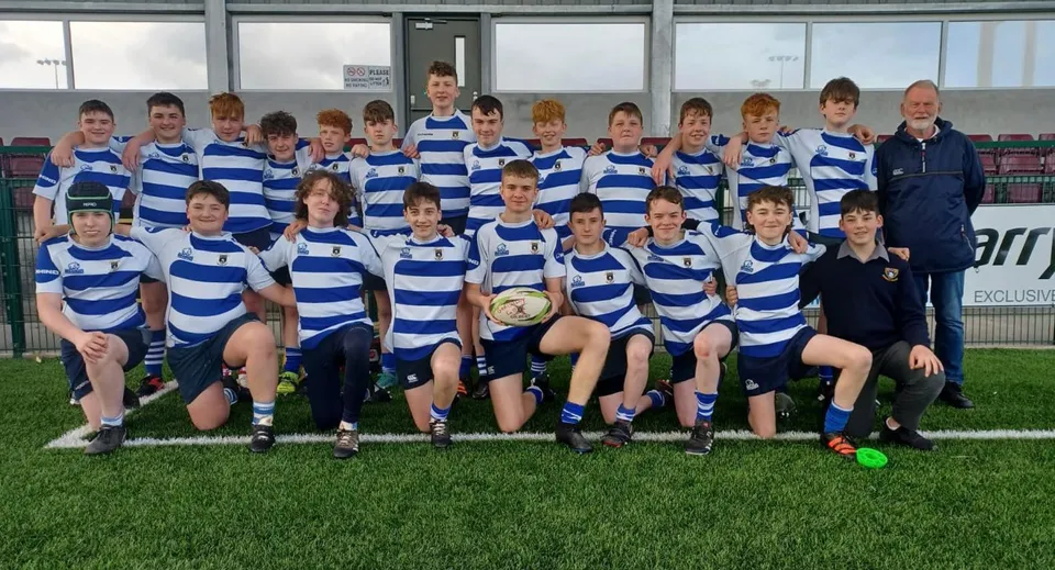 Un gruppo di giovani giocatrici di rugby del Garbally College è insieme su un campo da gioco davanti a un impianto sportivo.
