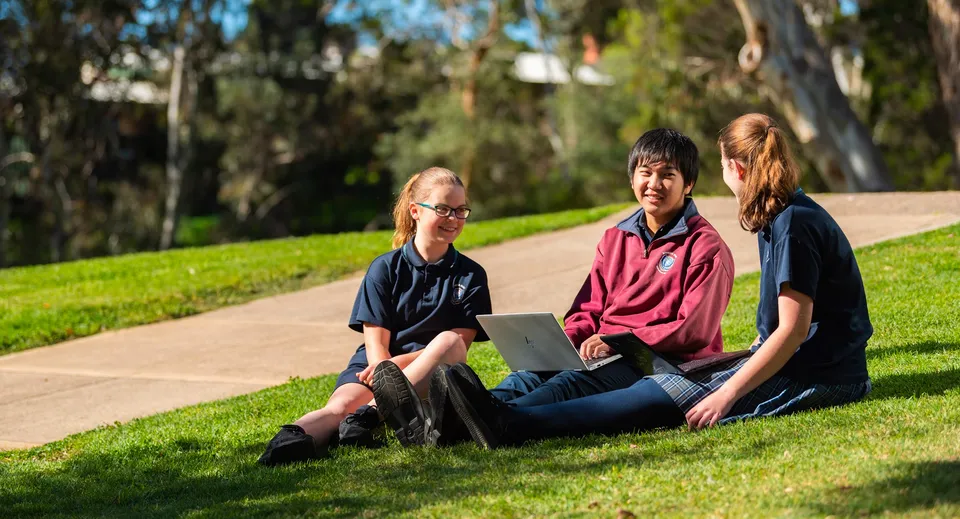Tre studenti della Banksia Park International High School siedono su un prato con alberi sullo sfondo.