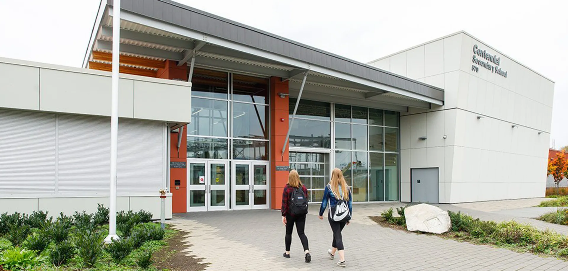 Due studentesse con zaini camminano verso l'ingresso moderno della Centennial Secondary School.
