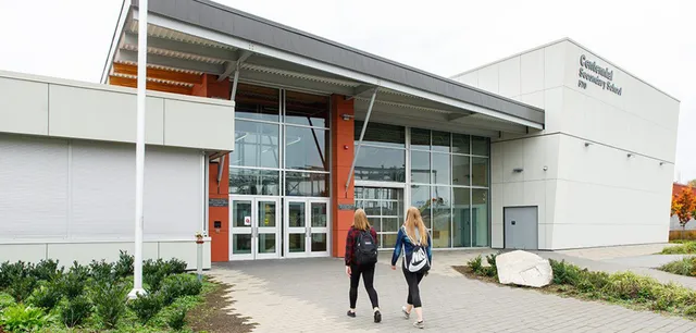 Due studentesse con zaini camminano verso l'ingresso moderno della Centennial Secondary School.