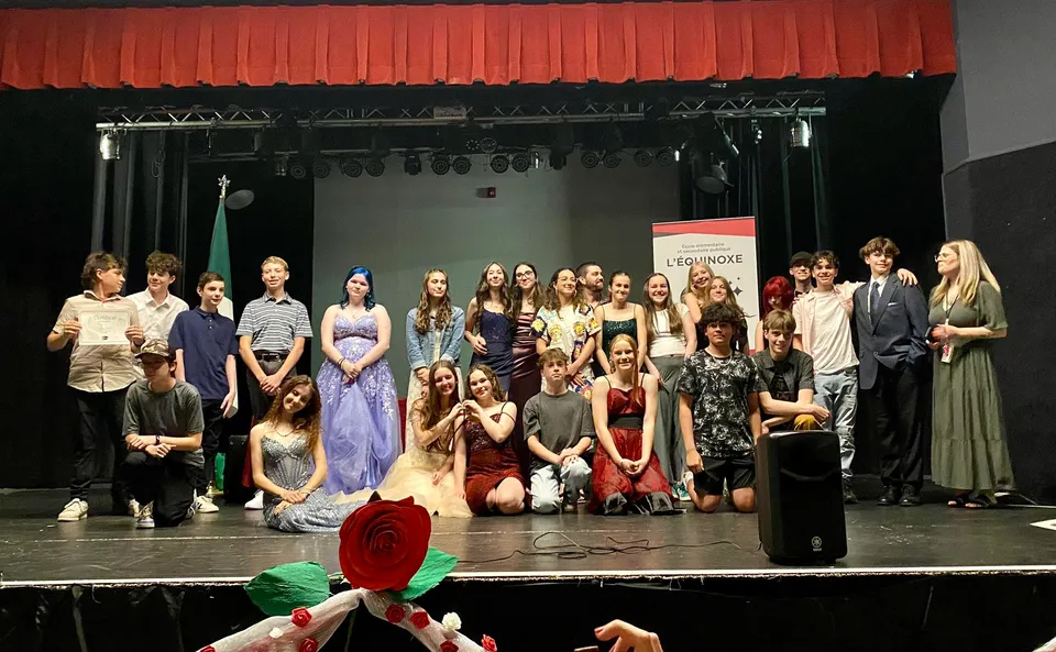 Un gruppo di studenti e studentesse in abito formale sul palco della École élémentaire et secondaire publique L'Équinoxe davanti a un sipario rosso.