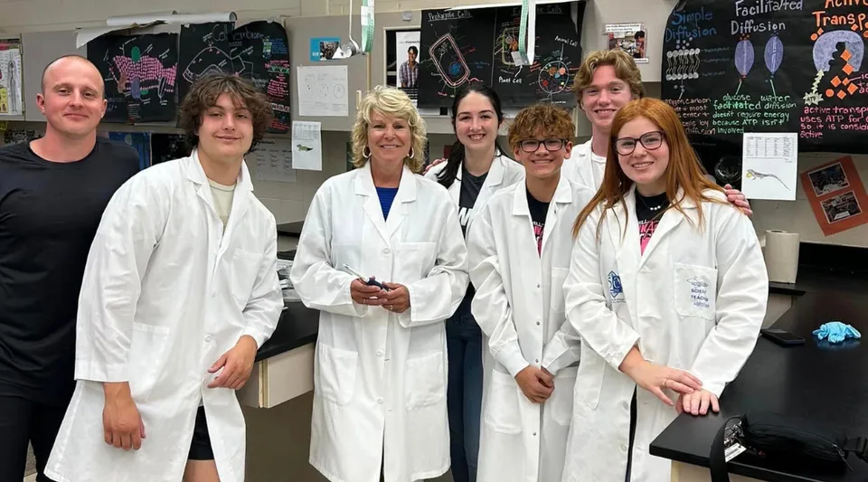 Gli studenti della Lowell High School sono insieme in un'aula con poster scientifici, indossando camici bianchi da laboratorio.