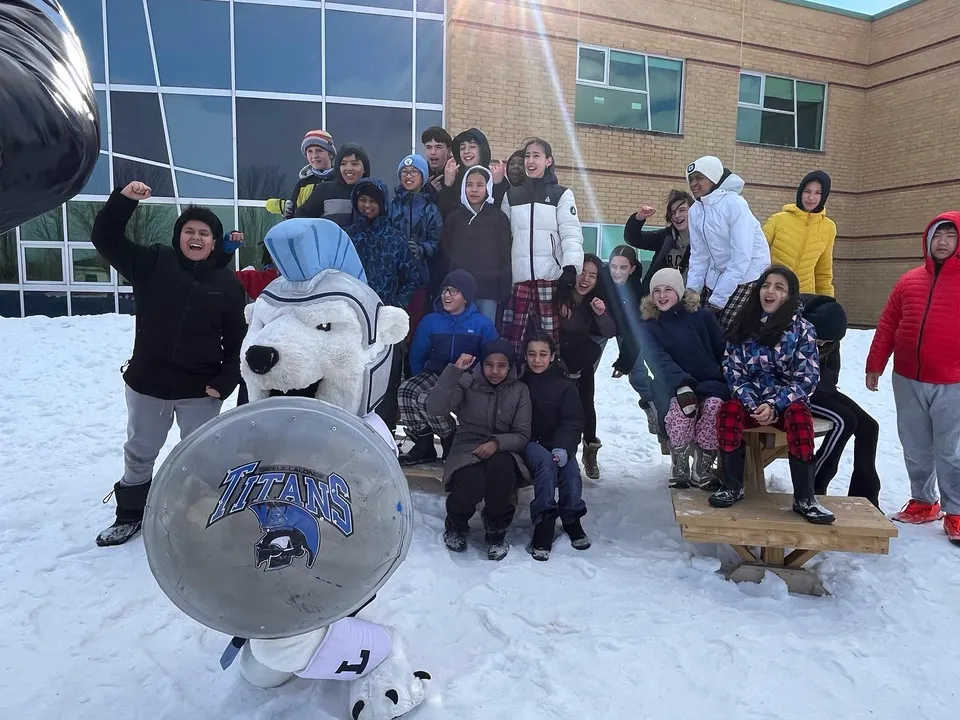Un gruppo di studenti e adulti è in piedi davanti all'edificio della École secondaire publique Gisèle-Lalonde con una grande mascotte gonfiabile.