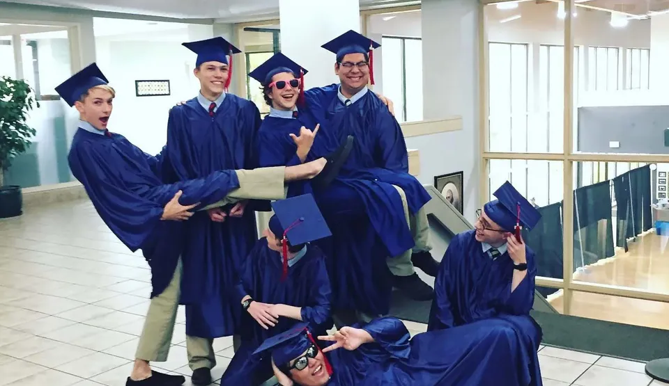 Un gruppo di diplomati della American Heritage Academy si trova nel corridoio con toghe e tocchi blu dopo la cerimonia di diploma.