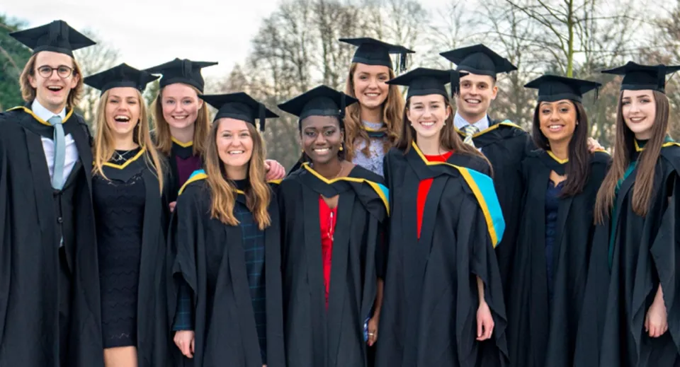 Un gruppo di diplomati della North Surrey Secondary School si trova all'aperto davanti agli alberi con l'abito da diploma.