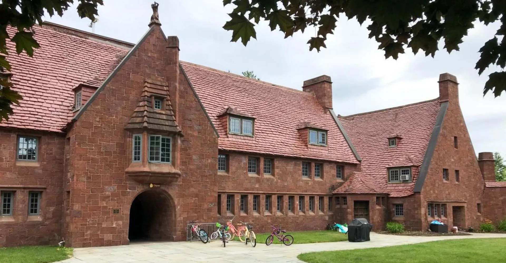 Il storico edificio in mattoni con tetto in tegole rosse della Avon Old Farms School è circondato da alberi e ciclisti.