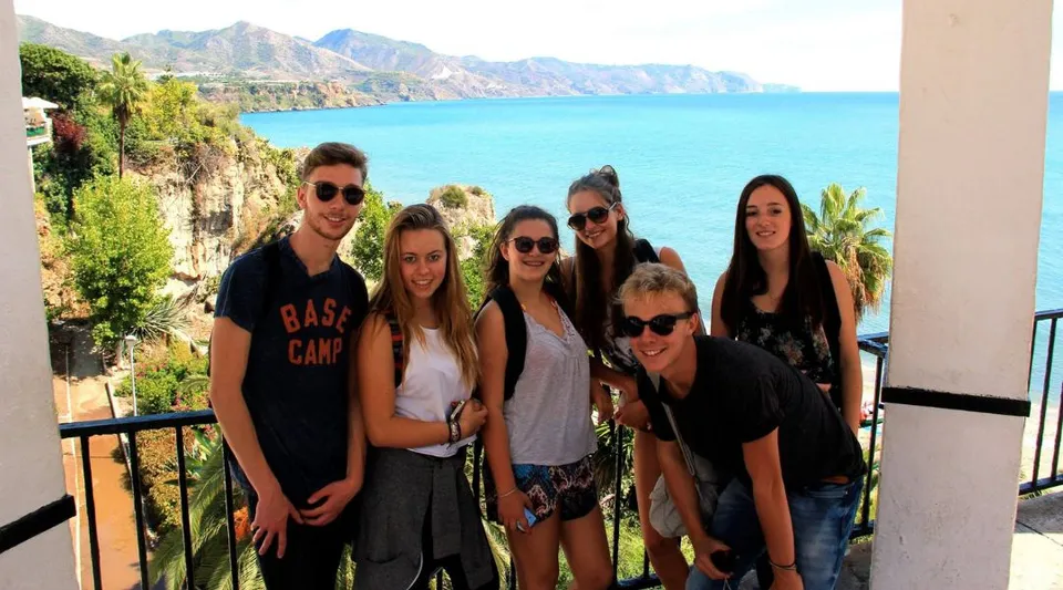 Un gruppo di studenti e studentesse del Lycée Jean Brito posa davanti a un paesaggio costiero con montagne e mare turchese.