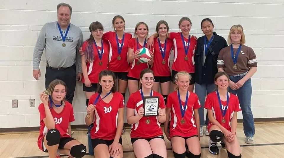 La squadra di pallavolo della Warner School posa in palestra con le allenatrici e un trofeo.