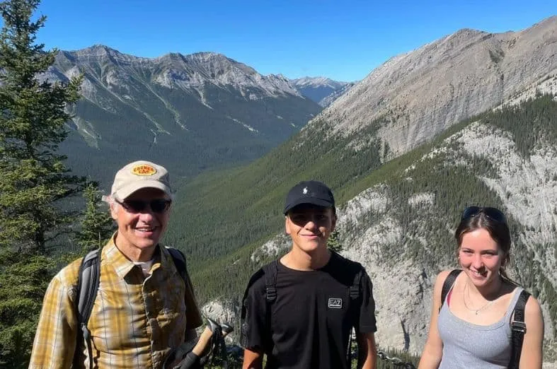Un hombre y dos jóvenes posan sonrientes ante un paisaje de montañas y valles