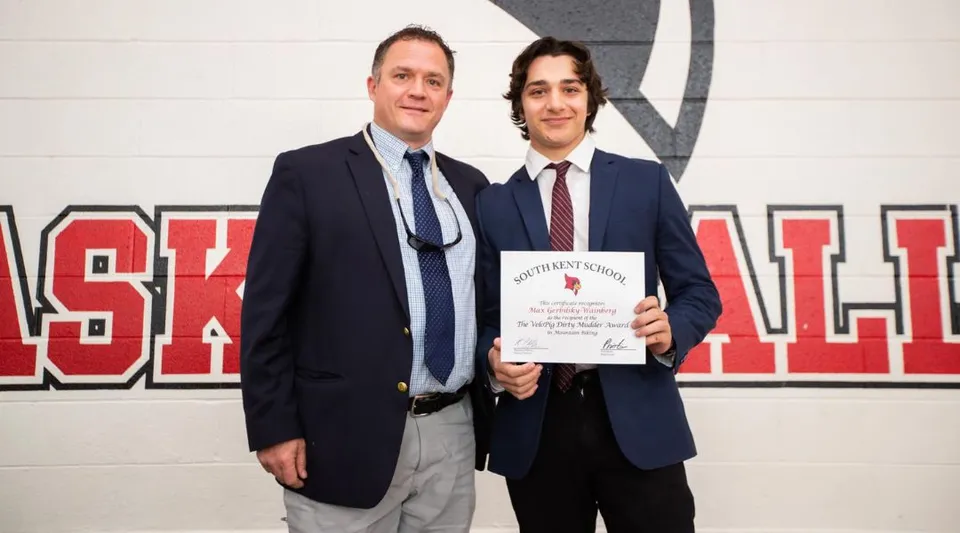 Uno studente della South Kent School tiene un certificato accanto a un uomo in giacca e cravatta davanti a una parete.