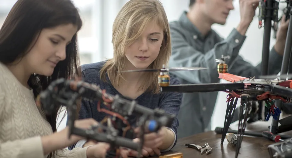 Tre studenti lavorano insieme a un dispositivo meccanico nell'officina del John F. Ross Collegiate Vocational Institute.