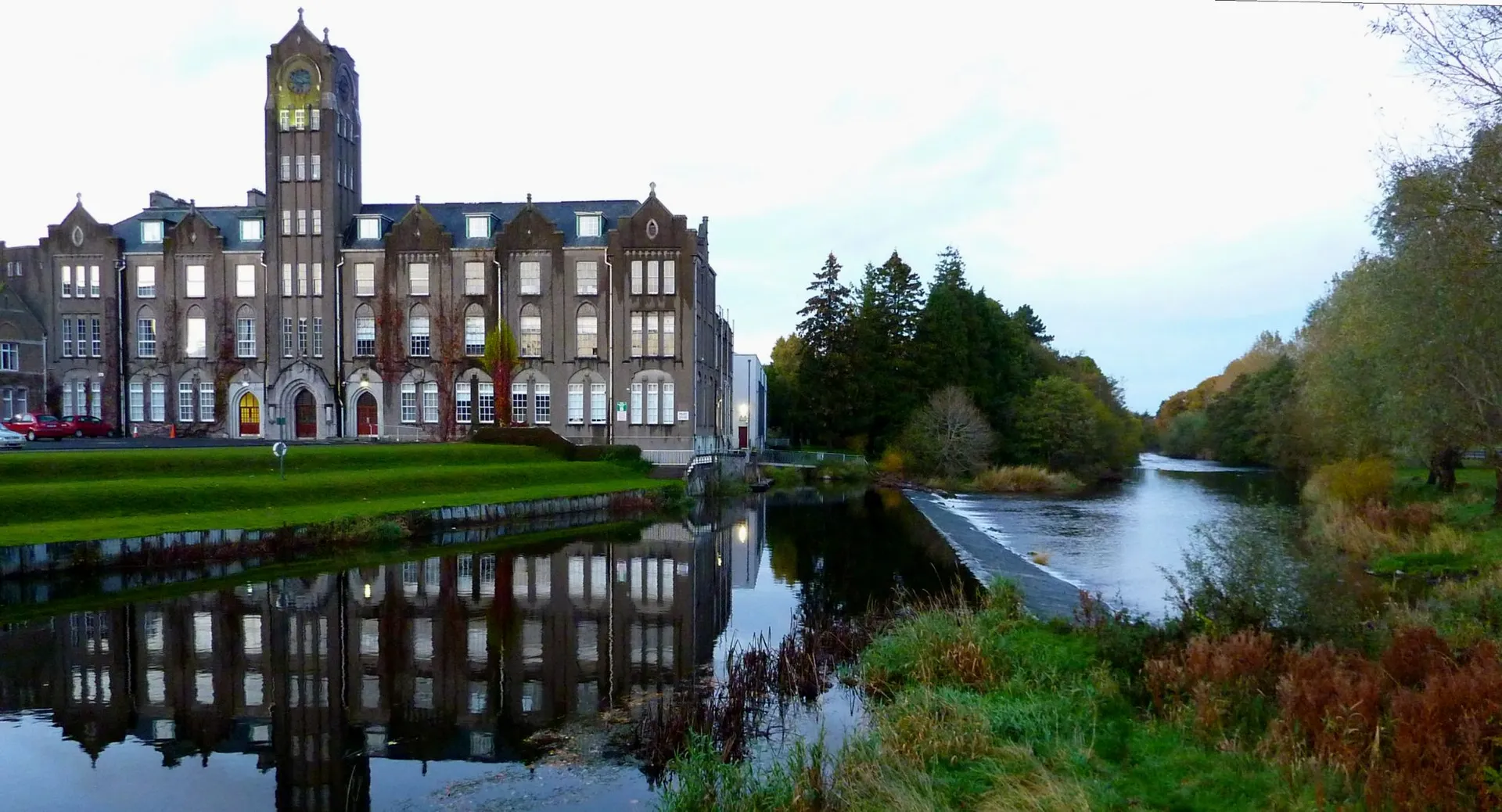 L'edificio storico del Newbridge College con un'alta torre dell'orologio si riflette nelle acque tranquille di un canale.