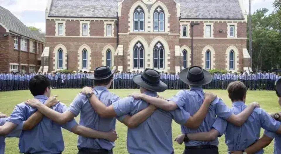 Studenti della Brisbane Grammar School in piedi davanti a un grande edificio in mattoni in stile gotico.