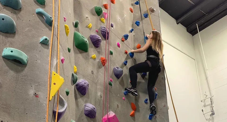 Uno studente o una studentessa della West Vancouver Secondary si arrampica su una parete di arrampicata colorata nella palestra.