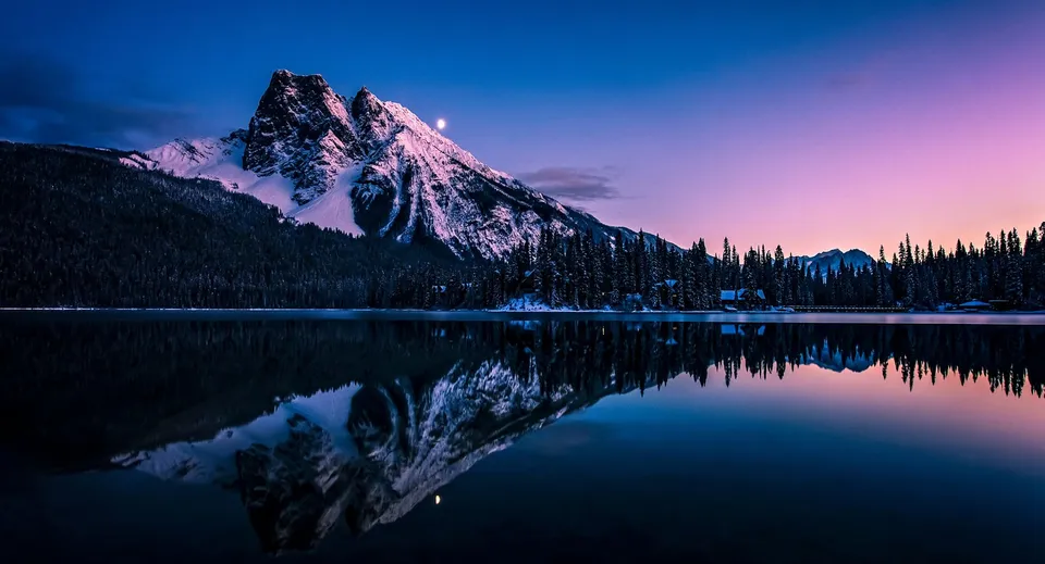 Un calmo lago di montagna riflette le cime innevate e il cielo serale nel paesaggio vicino alla Napanee District Secondary School.