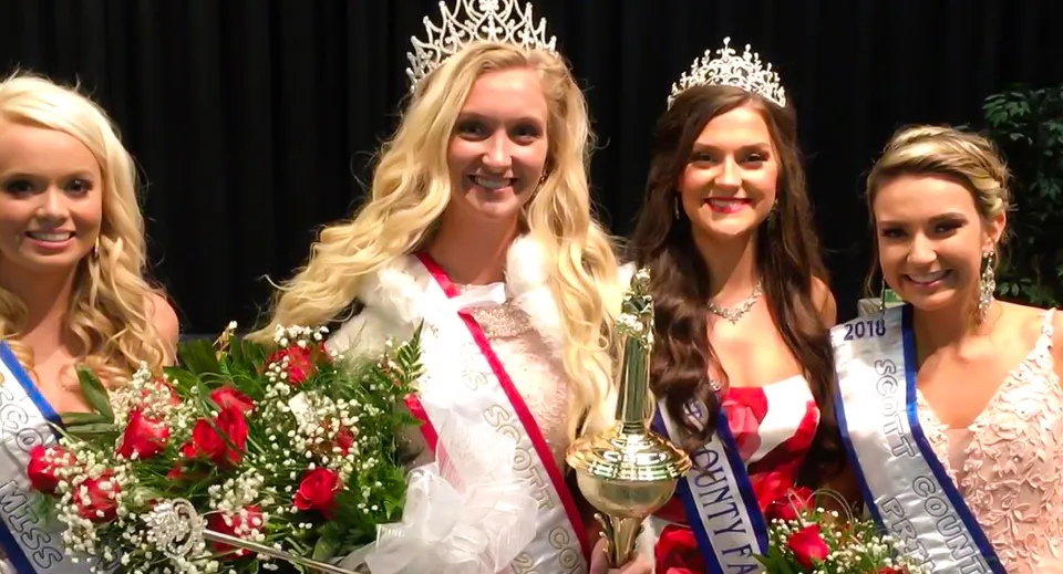 Quattro studentesse della Scottsburg High School con corone, fasce e abiti eleganti posano con un trofeo e dei fiori.