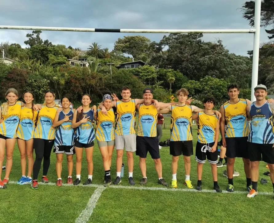 Un equipo deportivo de la Waiheke High School con camisetas amarillas y azules posa en un campo de césped.