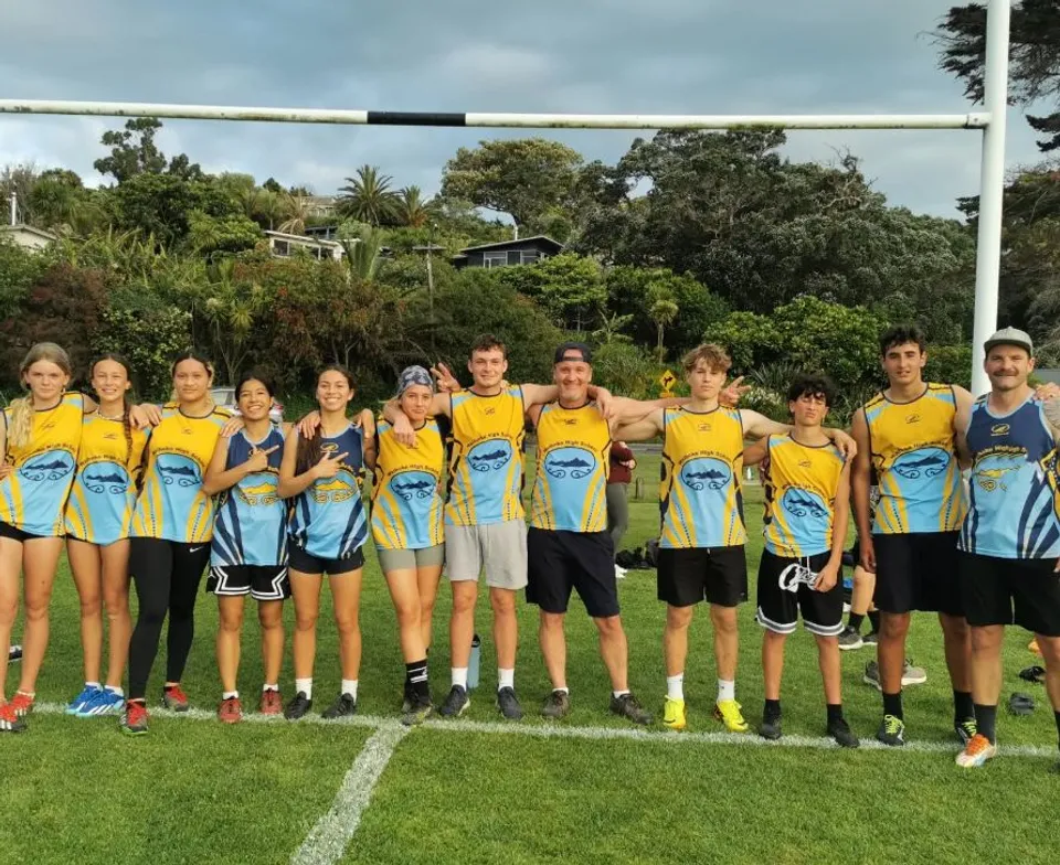 Una squadra sportiva della Waiheke High School con maglie gialle e blu posa su un campo da gioco in erba.