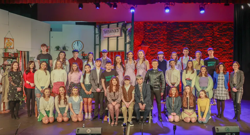 Un gruppo di studenti si trova sul palco del Holy Rosary College davanti a luci colorate e a una parete in mattoni.
