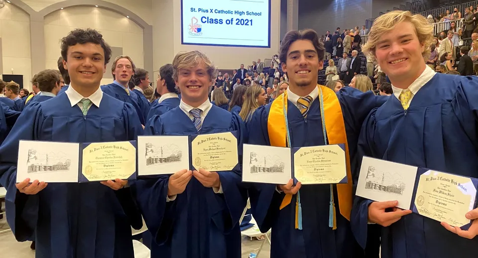 Quattro diplomati della St. Pius X High School in toga tengono i loro diplomi durante una cerimonia di diploma.