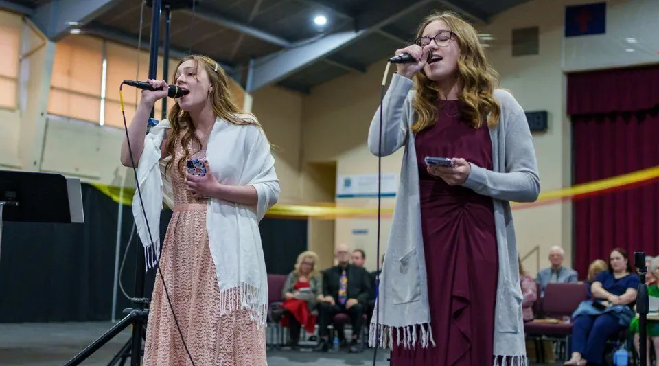 Due studentesse delle Overland Christian Schools cantano sul palco durante un'esibizione.
