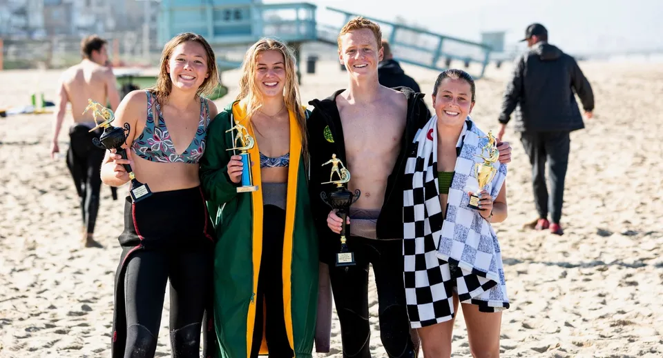 Un gruppo di studenti e studentesse della Clarence High School si trova sulla spiaggia con uno sfondo urbano.