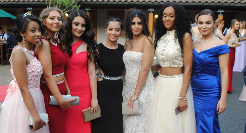 Un gruppo di giovani donne in abito formale si trova davanti a un edificio con tetto in tegole nel campus della Queen Mary's School.