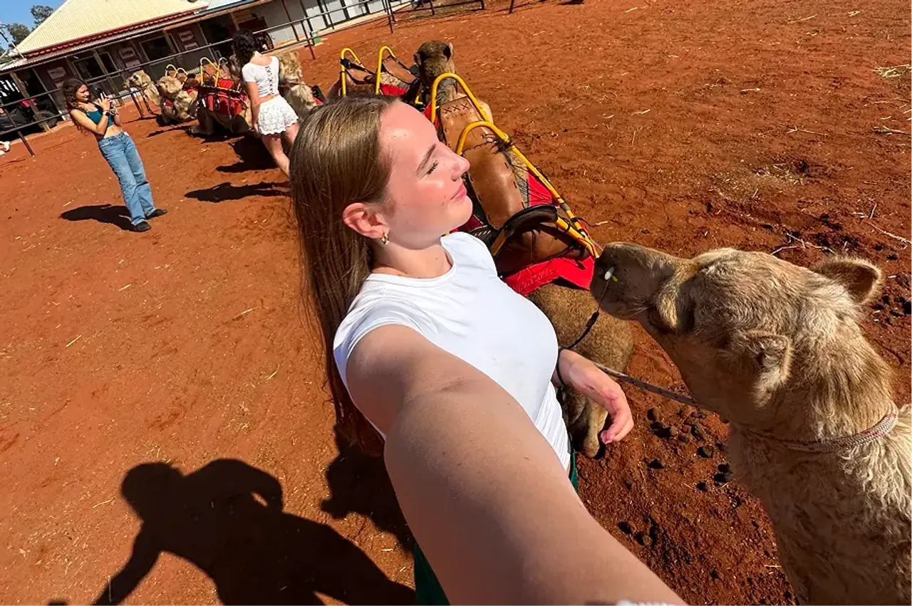 Studentessa si fa un selfie accanto a un cammello nell'outback australiano dalla terra rossa