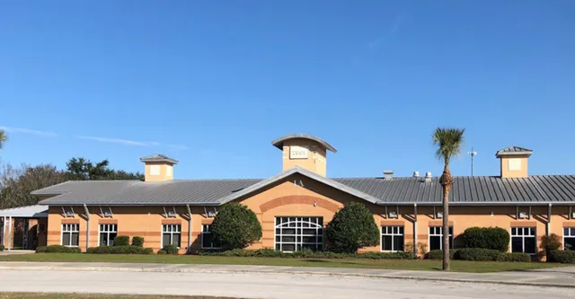 L'edificio in mattoni con tetto in metallo e ciminiere delle Marion County Public Schools è circondato da alberi e spazi verdi.