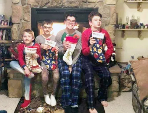 Cuatro jóvenes en pijama posan sentados frente a una chimenea encendida sosteniendo calcetines navideños