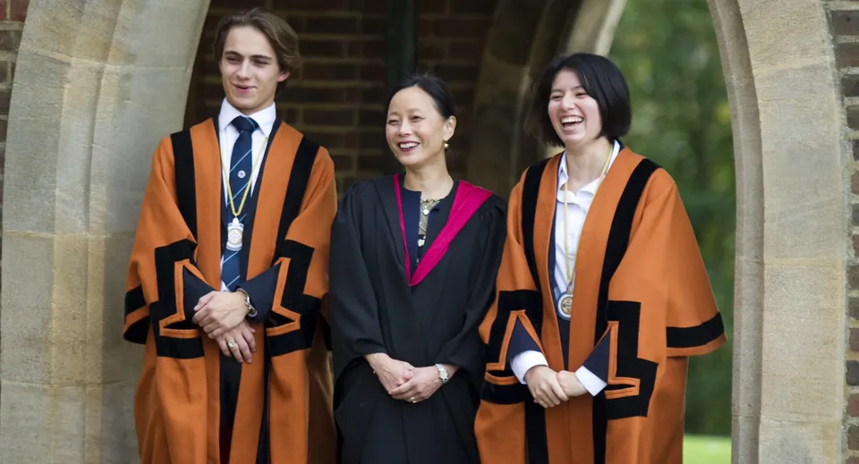 Tre persone in toghe accademiche si trovano davanti a un arco in pietra nel campus della King Edward's Witley School.