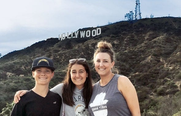 Tres personas sonríen juntas posando delante de la colina con el cartel de Hollywood