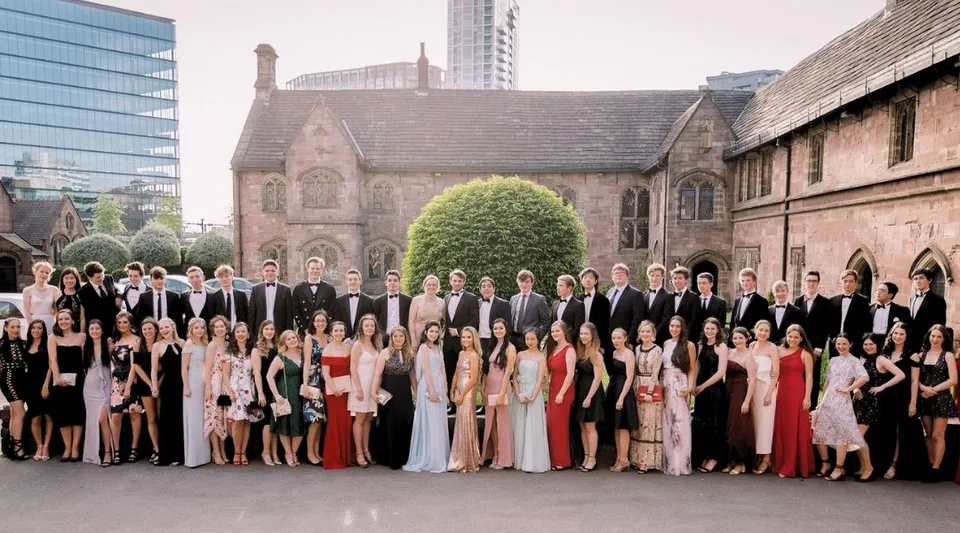 Un gruppo di persone in abiti formali sta davanti a una chiesa storica nel terreno della Chetham’s School of Music.